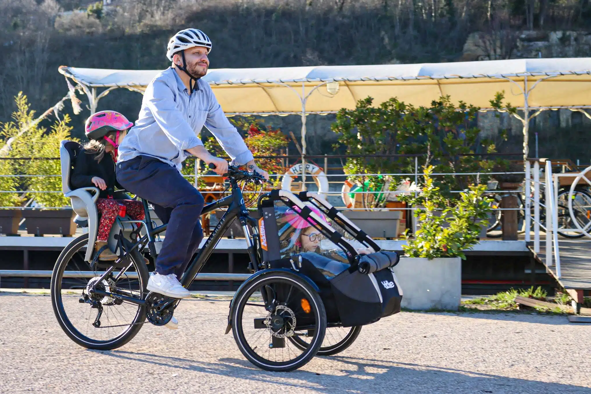 Bike family cargo accessory used by a dad with his daughters in a leafy urban area