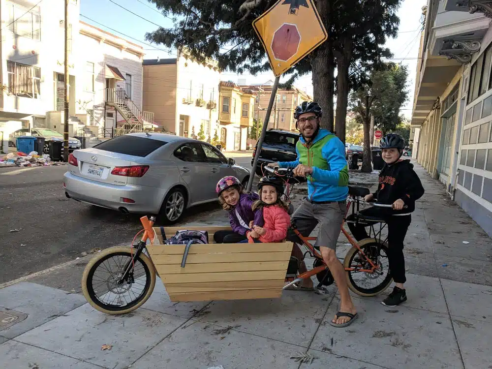 Lastenrad Umbau kit: selbstgebautes Lastenfahrrad, gefahren von einem Vater mit 3 Kindern